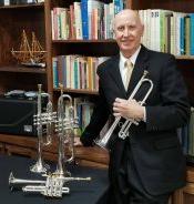 Man holding a trumpet standing next to a table with two additional trumpets on display at Howard Payne University. | HPU